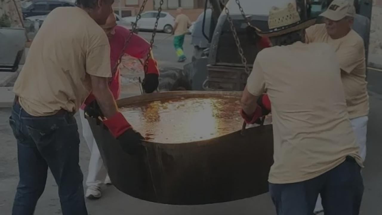 Imagen de varios hombres llevando una caldereta de rabo de toro con patatas