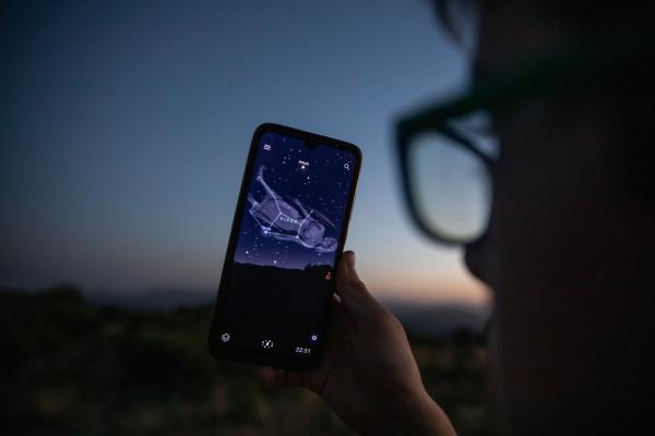 Imagen de una persona interpretando el cielo nocturno a través de un teléfono móvil